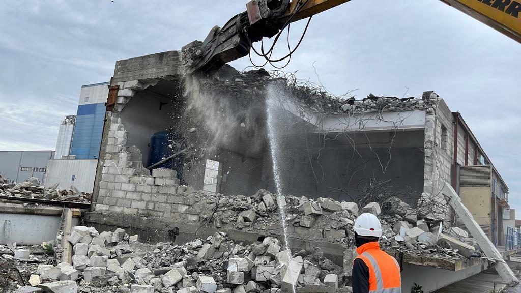 Mechanical demolition of a concrete-block industrial building with shears and water mist